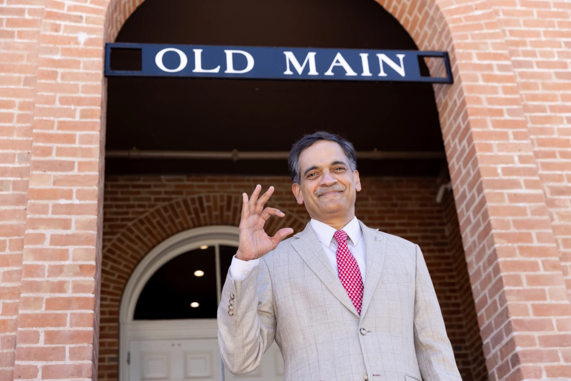 Image of President Garimella beneath a sign that says Old Main. He is making the WC hand gesture for Wildcats. 